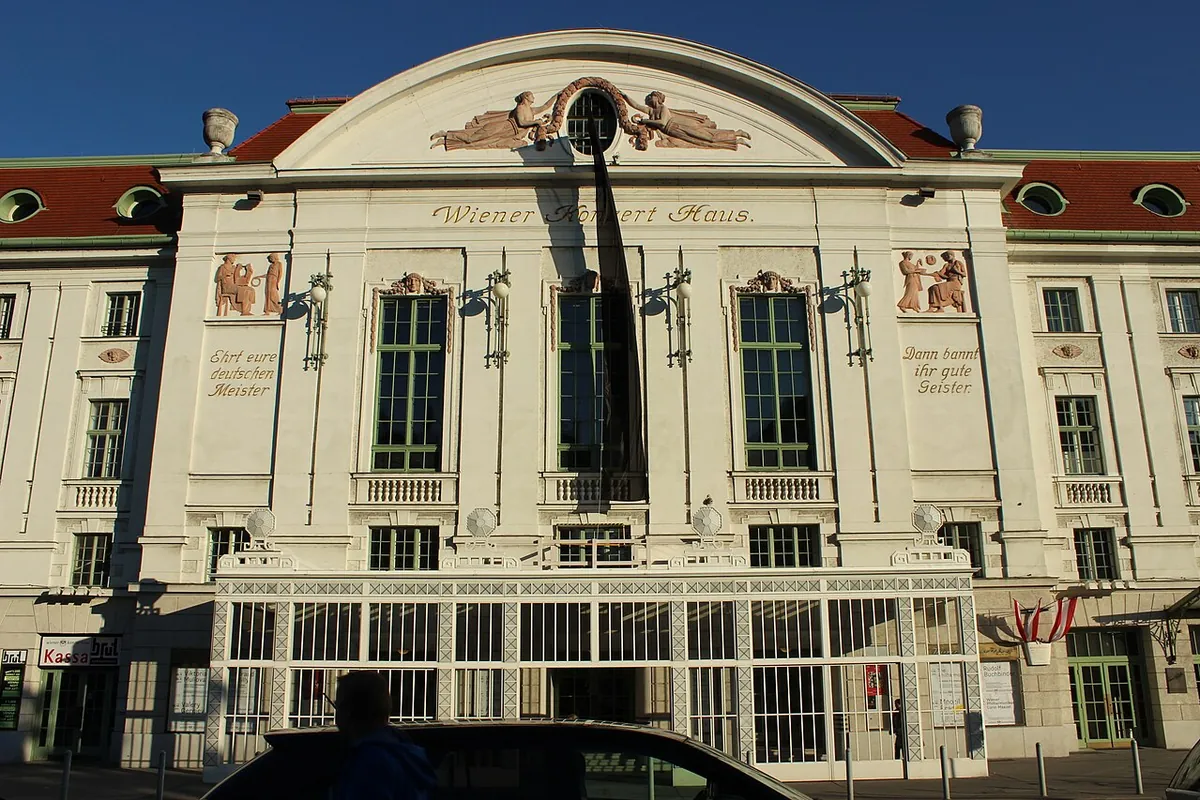 The front of the Wiener Konzerthaus, with a pale facade, a curved pediment, tall green-framed windows and a glass entrance canopy